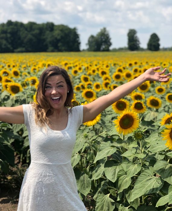 Happy Health and Life Coach, Arielle smiling in a field of sunflowers
