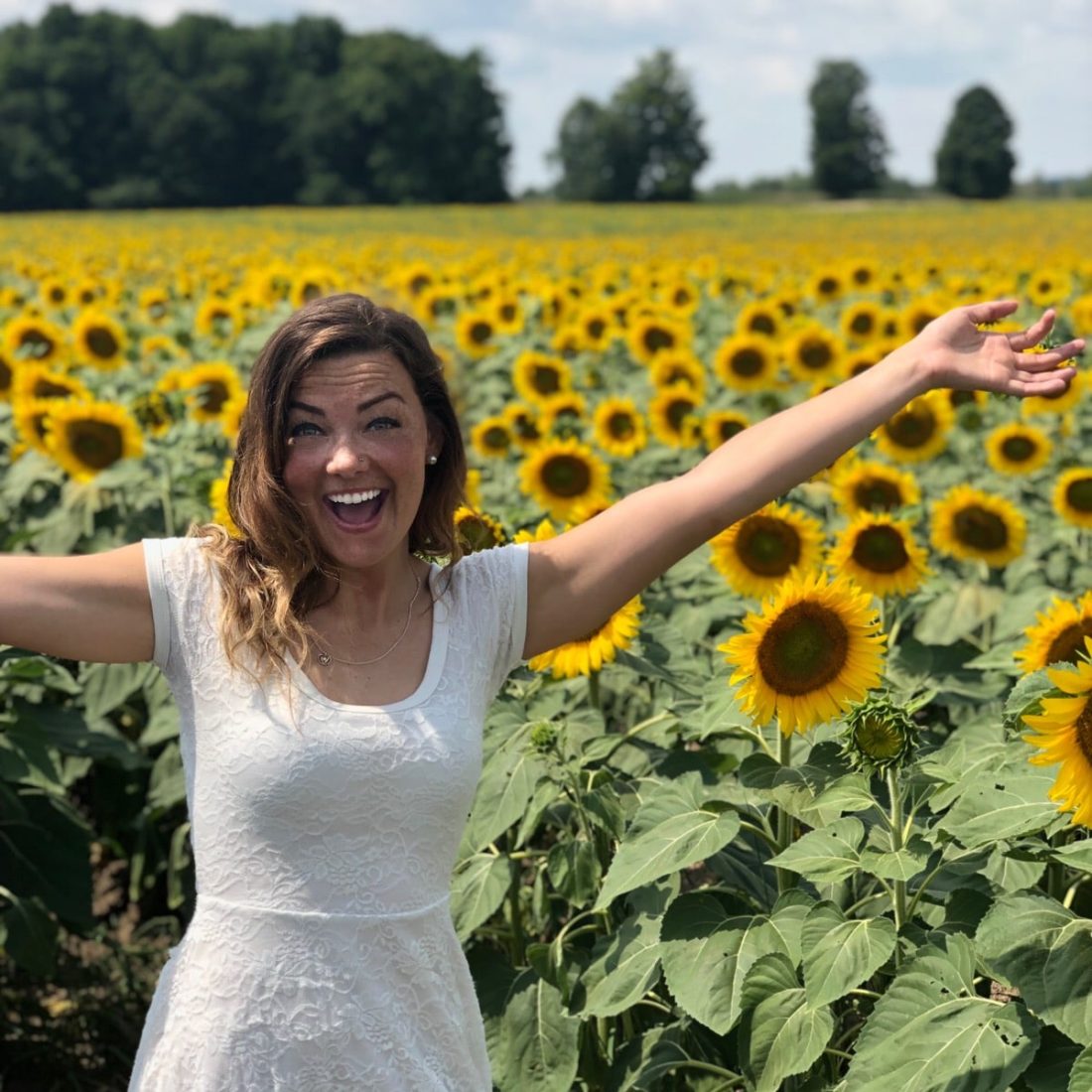 Happy Health and Life Coach, Arielle smiling in a field of sunflowers